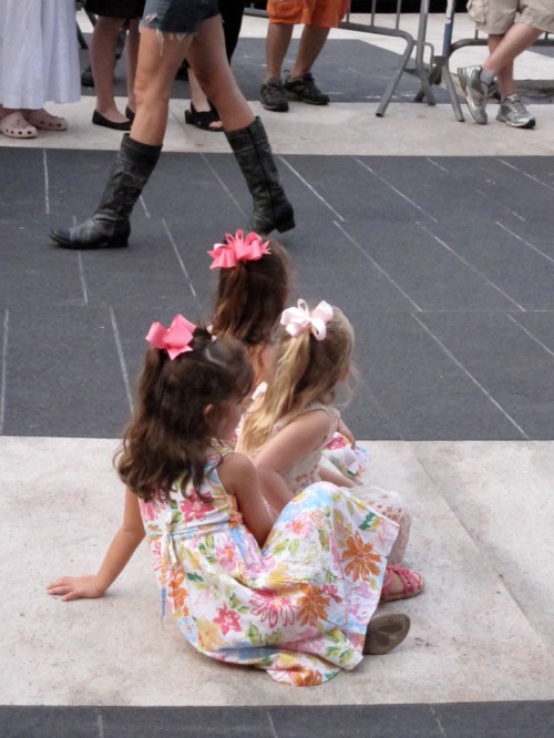 Three little girls sitting on Josie Robertson Plaza, mesmerized by Asphalt Orchestra.